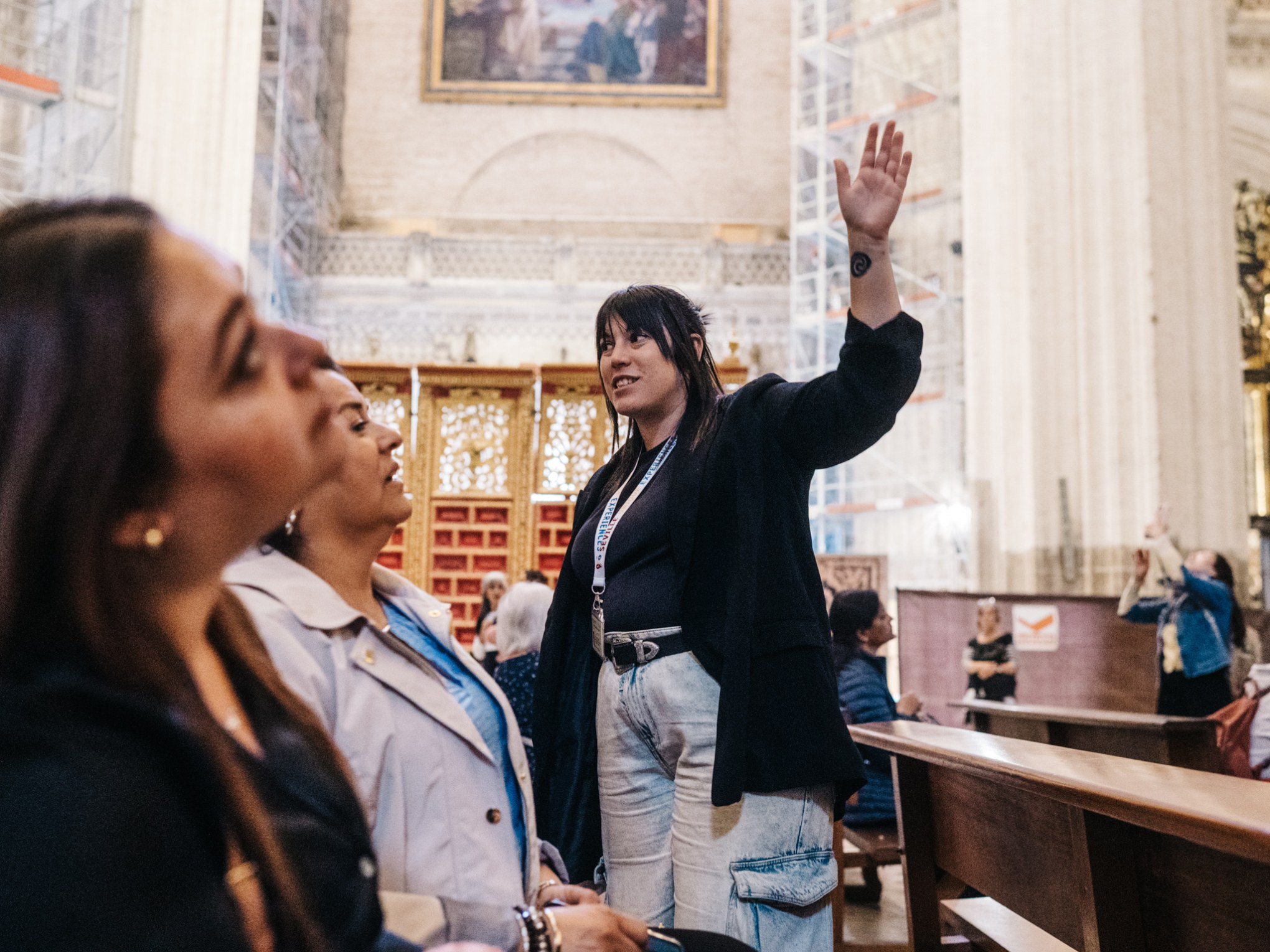 A tour guide gestures upward in a cathedral while speaking to visitors.