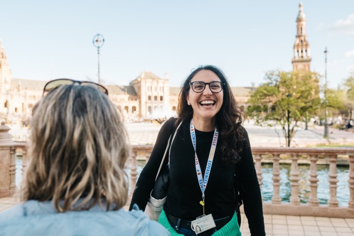Woman smiling outdoors with a historic building in the background.