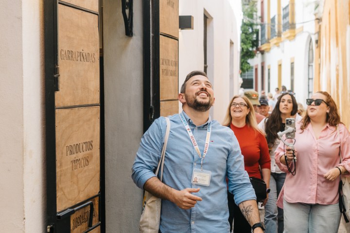 People walking cheerfully past a shop in a narrow street.