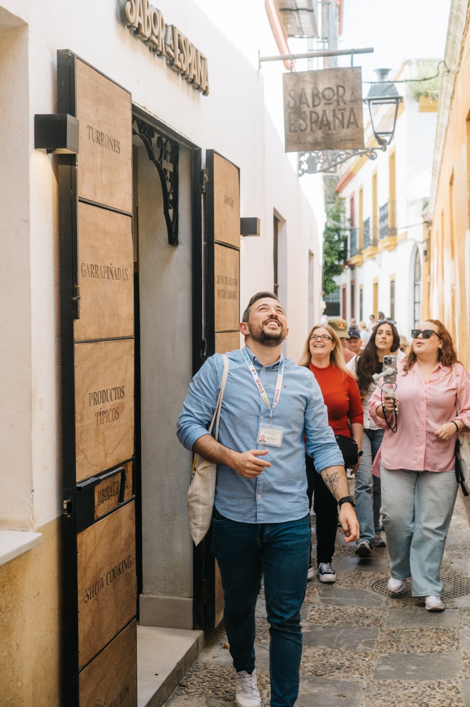 People walking cheerfully past a shop in a narrow street.