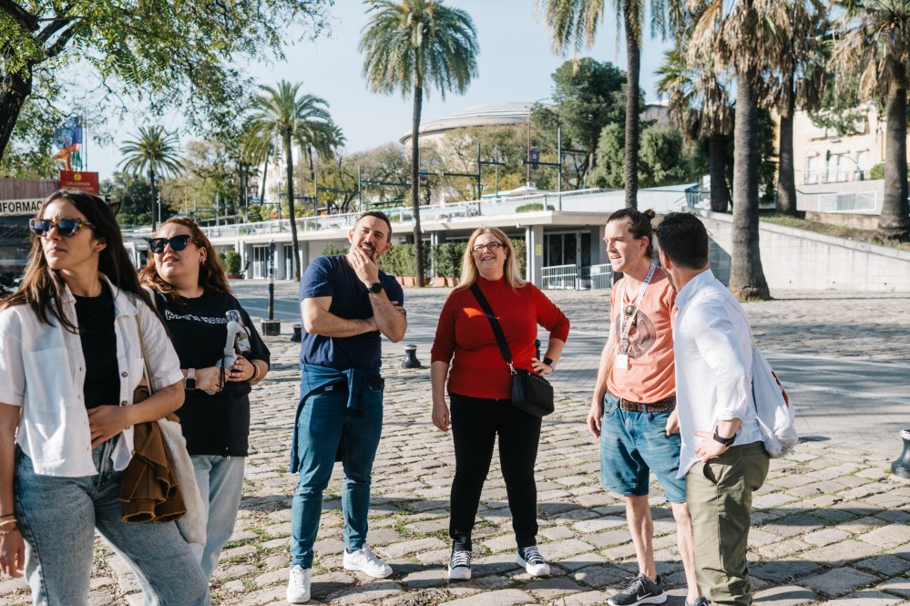 Group of six people standing outdoors, surrounded by palm trees on a sunny day.