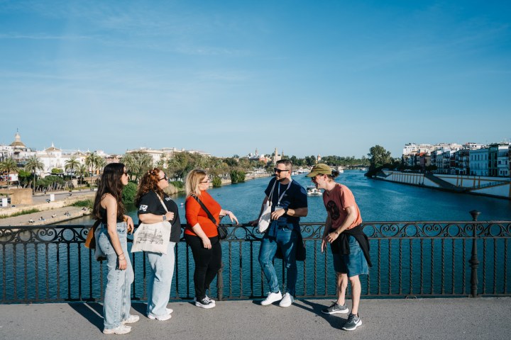 Five people conversing on a bridge overlooking a river and city skyline.
