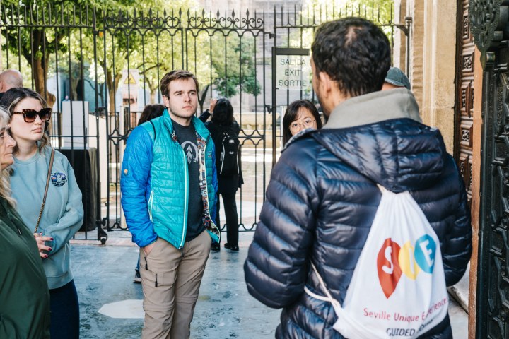 Group of tourists listening to a guide near a gated entrance.