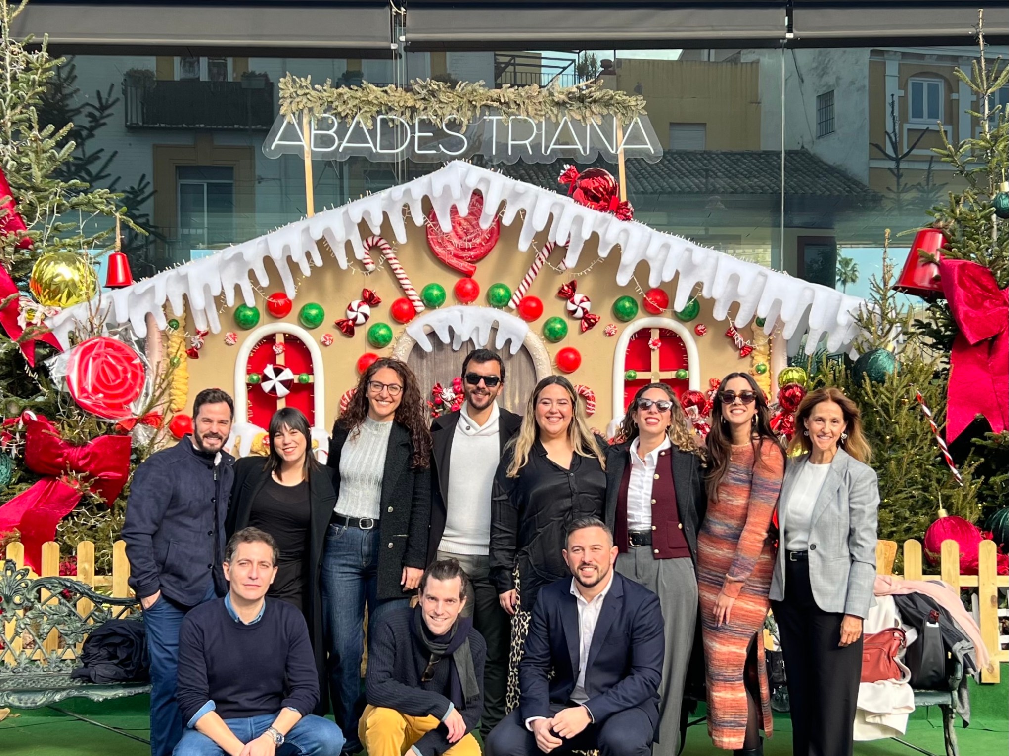 Group of people posing in front of a festive gingerbread house display with decorations.