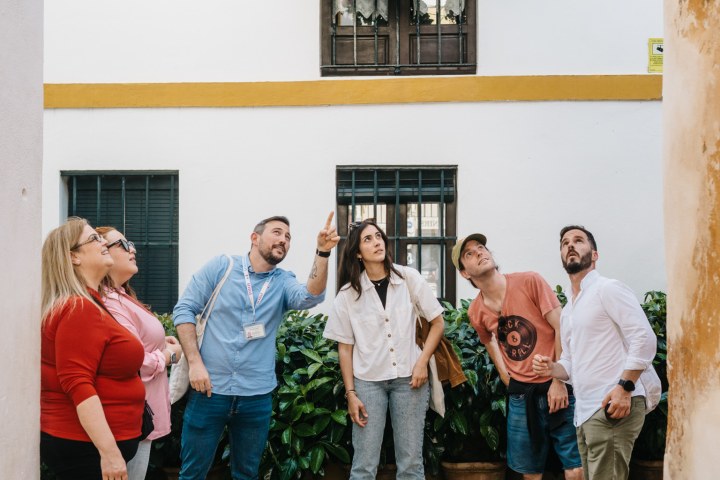 Group of people standing in a courtyard, looking up at a flowered window box.
