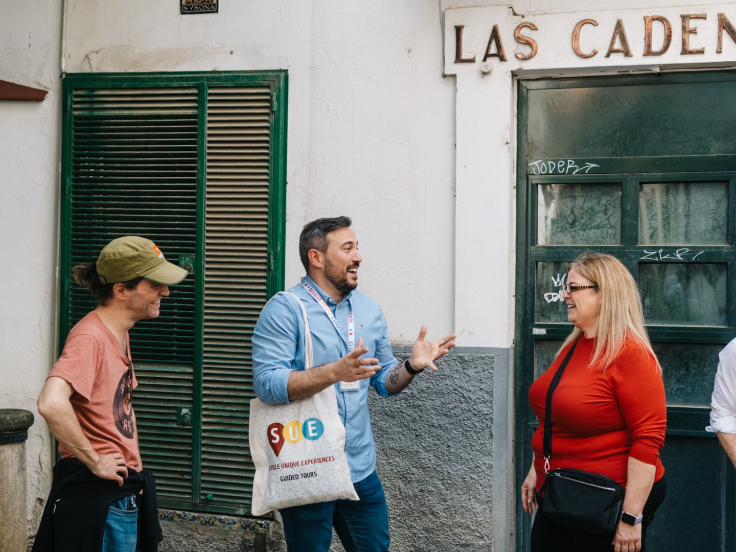 Three people talking outside a building with a 'Las Cadenas' sign above.