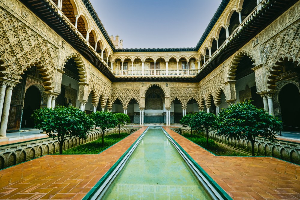 Ornate courtyard with arches and trees around a narrow reflecting pool.