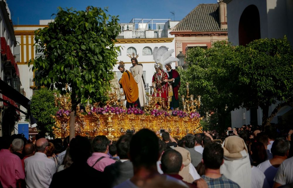 Large crowd watching a religious procession with ornate statues outdoors.