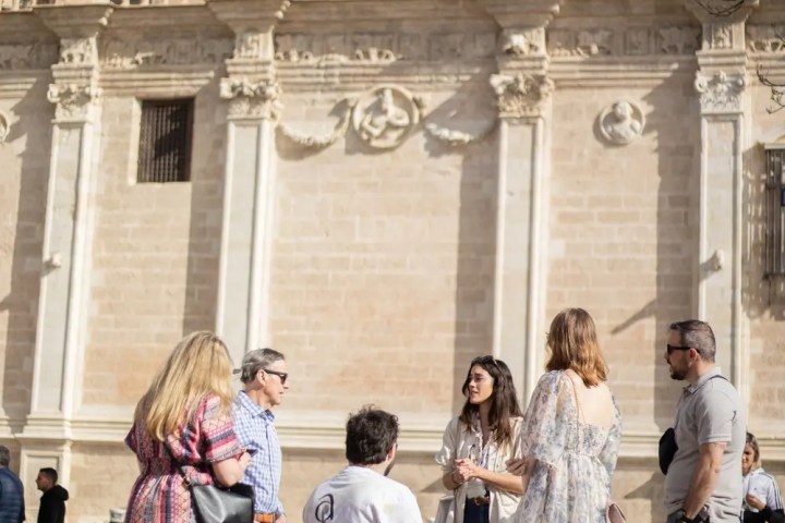 Group of people, including a person in a wheelchair, chatting outside a historic building.