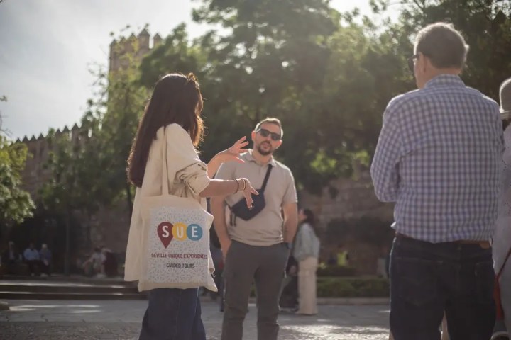 People conversing outdoors with a tote bag and greenery in the background.