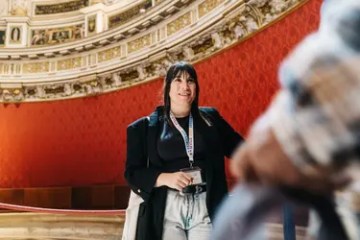 Smiling person with badge in an ornate room with red walls.
