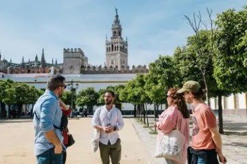 People talking in a plaza with a tall historic tower in the background.