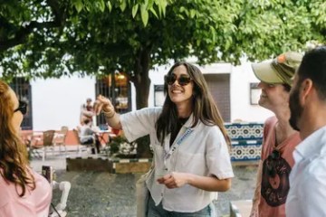 Group of people smiling outdoors, one woman in sunglasses holding an item.