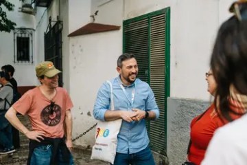 Group of people talking and smiling outdoors near a white wall.