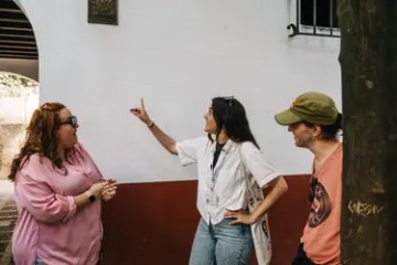 Three people talking and gesturing near a white and red wall.