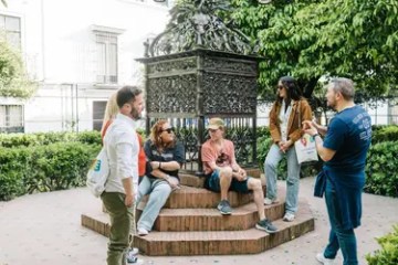 Group of people sitting around a small, ornate monument in a garden setting.