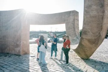 People standing near large stone sculptures with a bridge in the background.