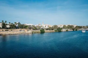 Riverside view with buildings and a boat under a clear blue sky.
