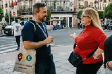Two people talking in a lively urban street setting.