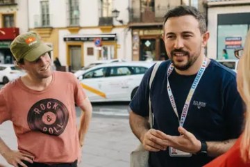 Two men talking on a city street, one wearing a cap and the other a lanyard.